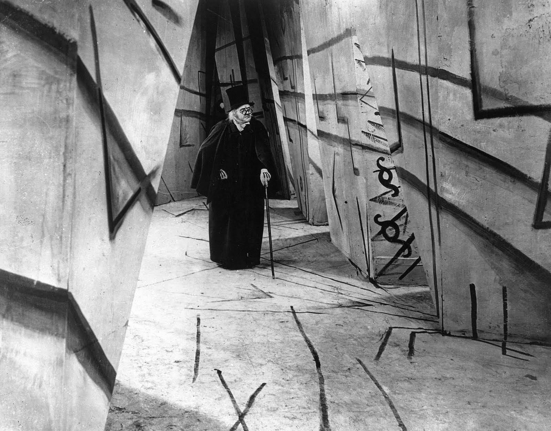 En svartvit stillbild från den tyska expressionistiska filmen 'Das Cabinet des Dr. Caligari' som visar en karaktär i en korridor med förvrängda väggar och golv.