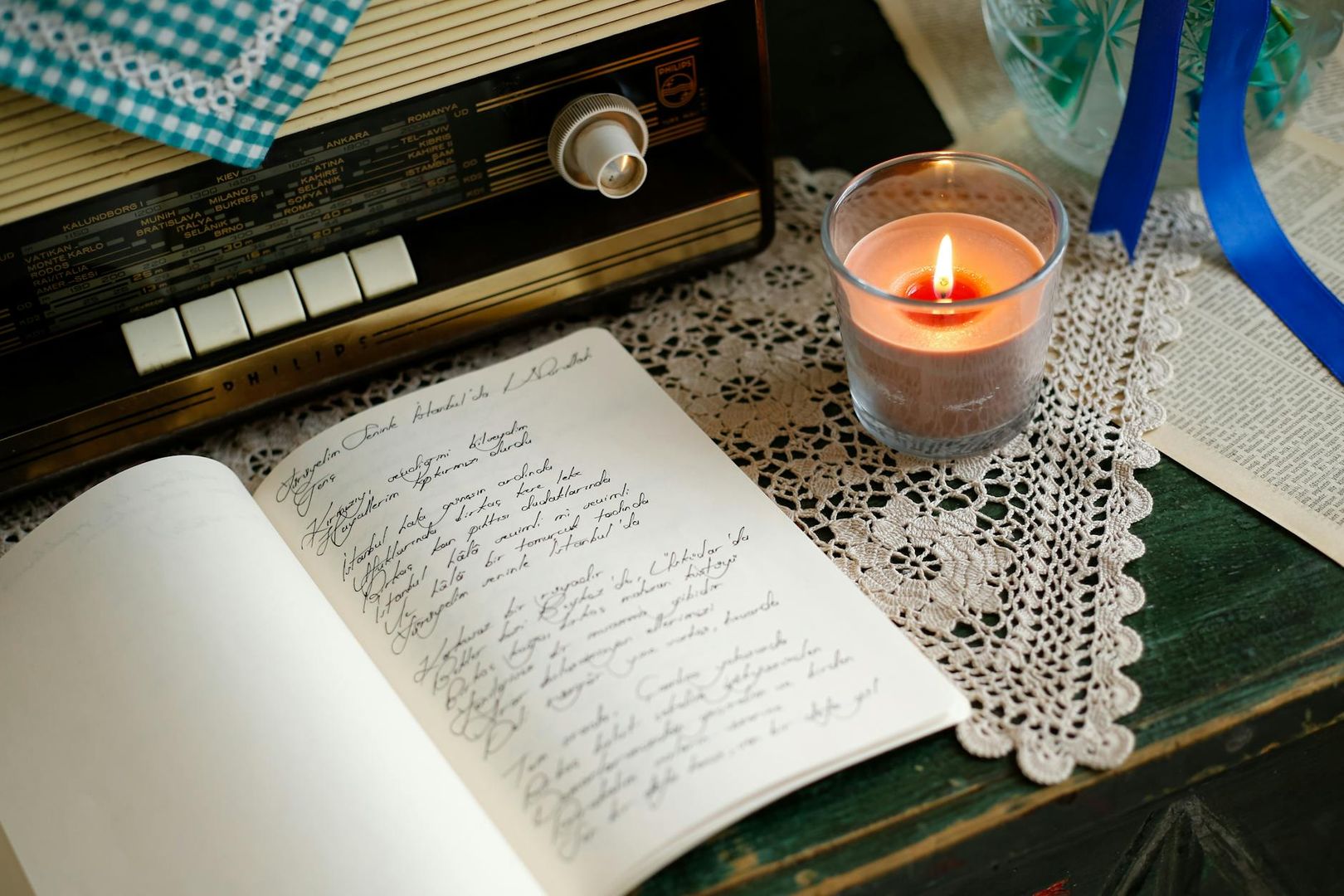 Anteckningsbok, tänd ljus och gammal radio på virkad duk.